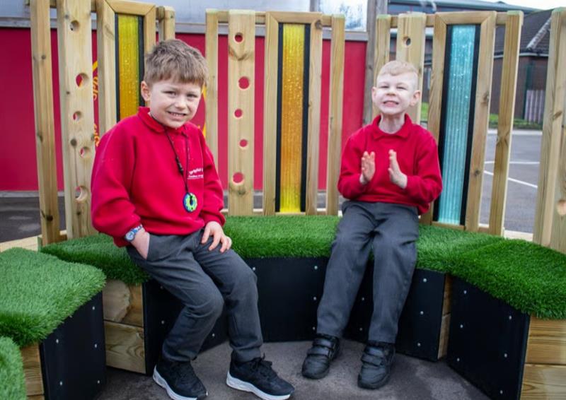 Two young boys sitting on grass topped seats in a school playground